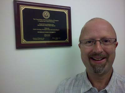 Dr. Josh Meisel, Director of the Practicing Sociology Track at Humboldt State University, recipient of the first graduate program accreditation by the Commission on the Accreditation of Programs in Applied and Clinical Sociology, shown with his CAPACS accreditation plaque